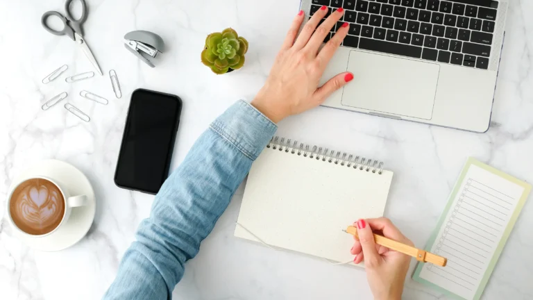 Flatlay of a desk scene with a women's hand on the computer keys as she searches for a recruitment company.